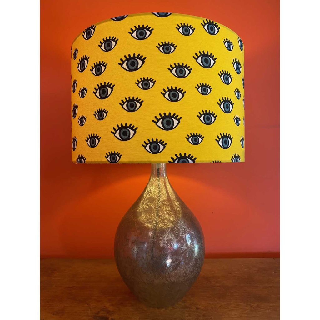 Lampshade by Orange Frog, featuring graphic 'eyelashed' eyes in grey on a mustard yellow background.