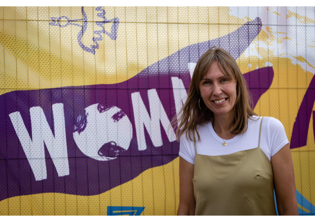 Paula Henderson of WOMAD standing in front of a WOMAD banner