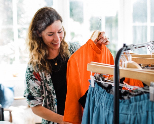 Amelia Twine holding up an orange t-shirt from a rack of clothes