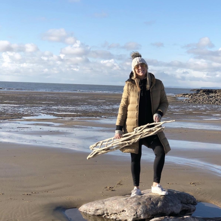 Amy of Weave Love Amy, collecting driftwood on a beach.