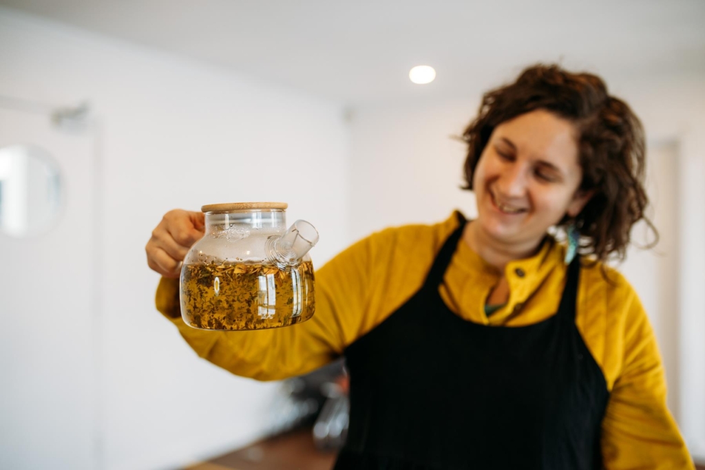 Ellen Rowland of Amberluna holding a clear teapot of steeped herbs