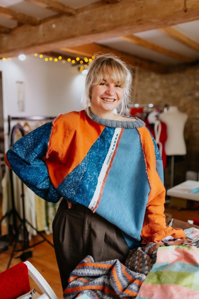 Evie in her Daines Atelier studio wearing blue and orange asymmetric top made from patchwork of vintage textiles