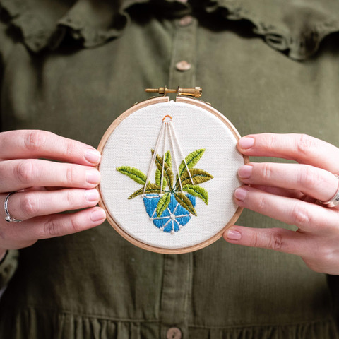 hand holding an embroidered hanging plant picture in a circular embroidery hoop