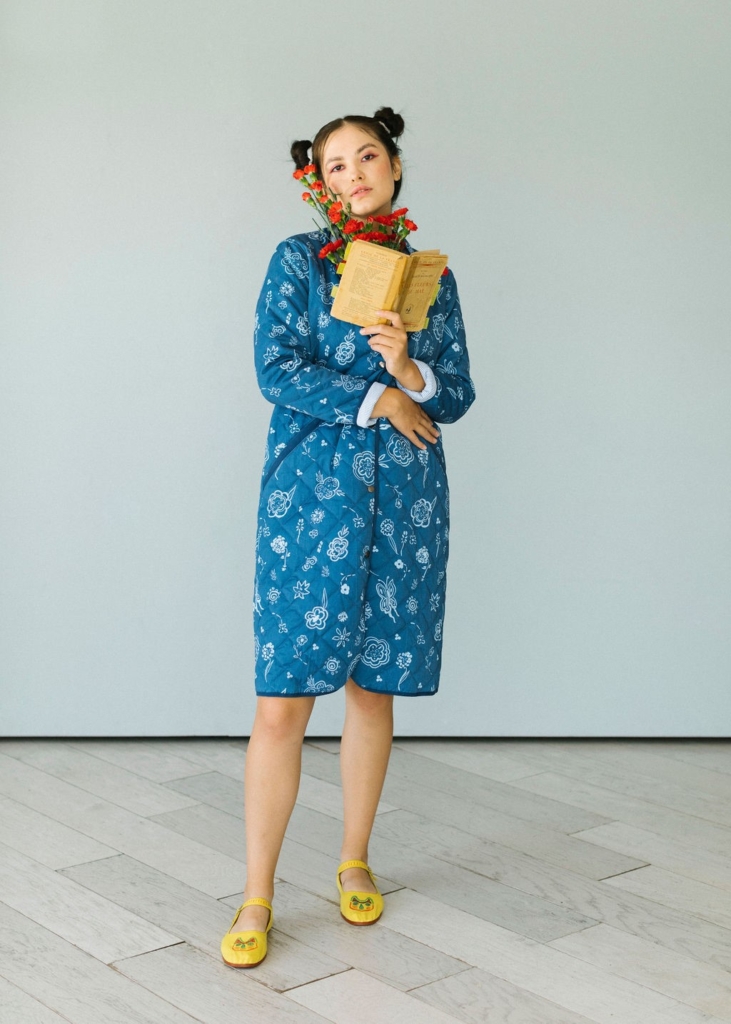 model wearing blue quilted chinese style coat with rounded seams and designs in white