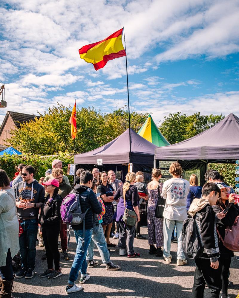 Sunny scene at Windmill Hill Market, with people shopping at stalls, and flags flying