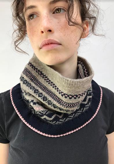 Model wearing 'Hook Norton' by Cotswold Knits - a patterned woollen snood in shades of stone grey, navy and pale pink.