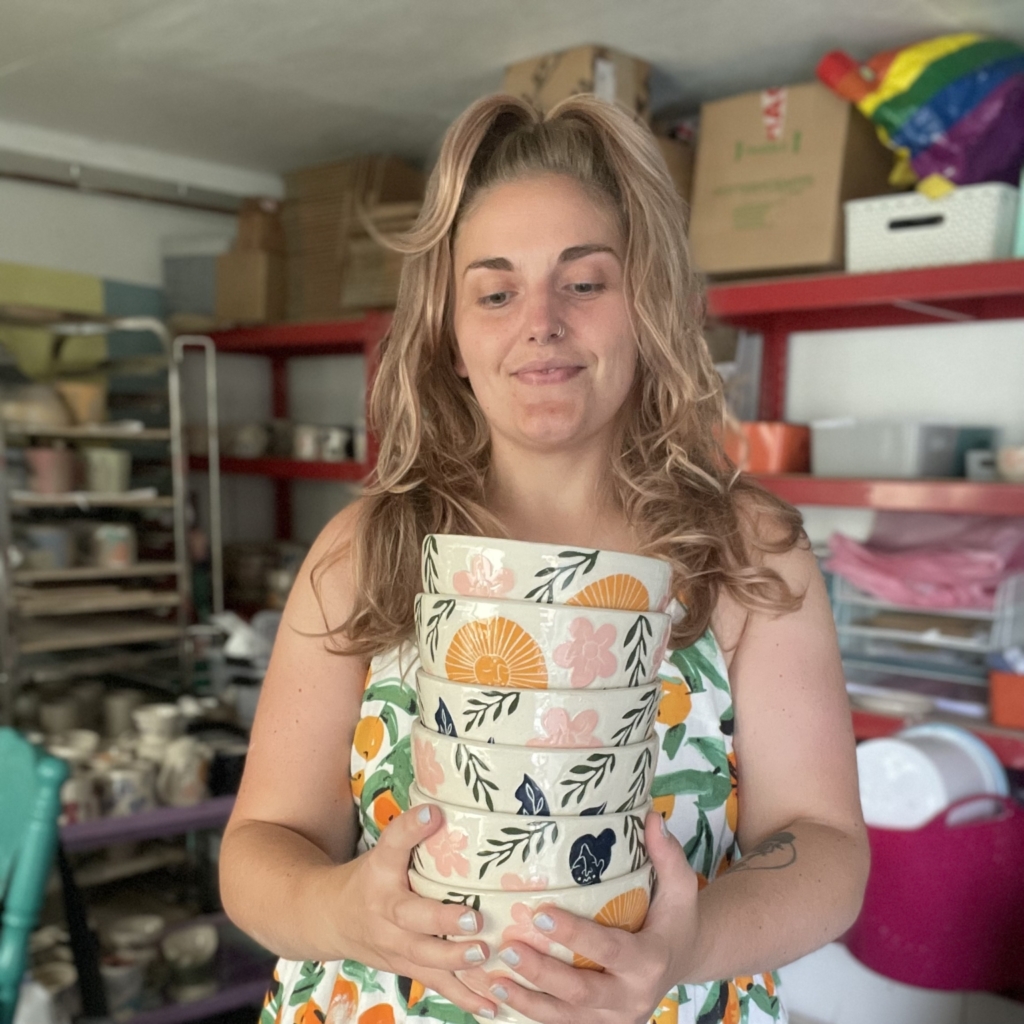 Angharad of Crock Â Shwt ceramics holding 6 large ceramic bowls brightly decorated with organic shaped floral designs in pink, orange and navy.