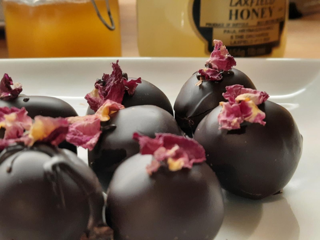 Group of dark truffle chocolates topped with a pink rose petal, by Vicolo Sei.