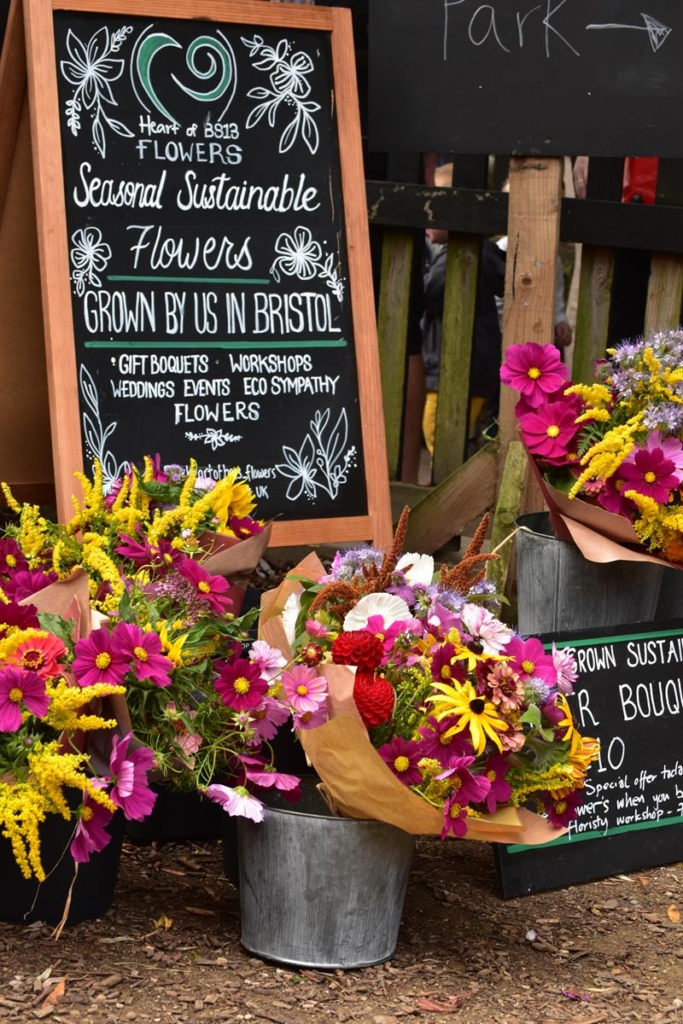 Flower stall with brightly coloured bouquets, and a blackboard saying 'Heart of BS13 Flowers' - Seasonable Sustainable Flowers Grown by us in Bristol.