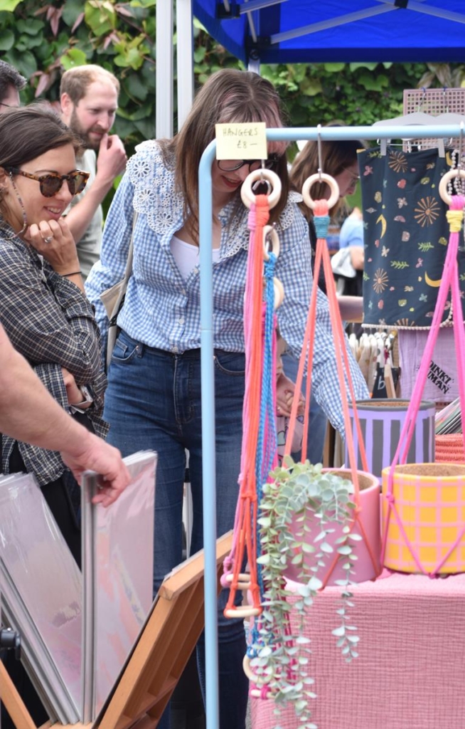 Shoppers at a market stall selling brightly coloured macrame hangers.