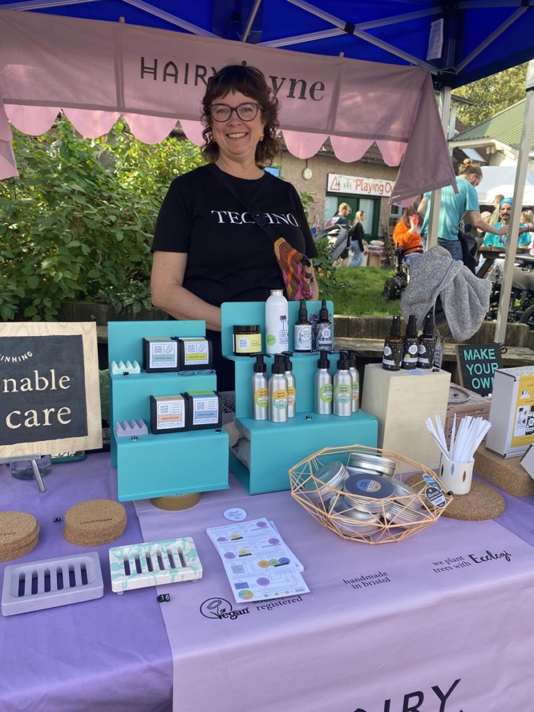 Hairy Jayne's market stall. Jayne is behind the stall, smiling, with her range of natural sustainable hair products, attractively packaged.