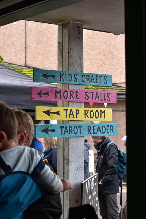 Wooden signs at Windmill Hill Market, pointing to Kids Crafts, More Stalls, Tap Room, and Tarot Reader.
